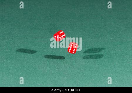 Two red dices falling on a green table Stock Photo