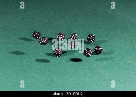 Ten black dices falling on a green table Stock Photo
