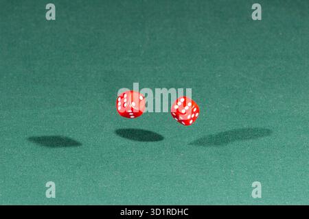 Two red dices falling on a green table Stock Photo