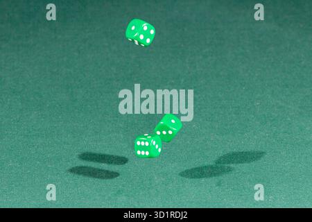 Three green dices falling on a green table Stock Photo