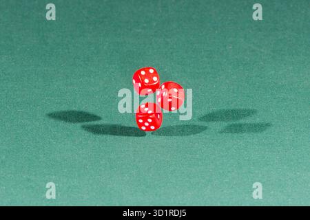 Three red dices falling on a green table Stock Photo