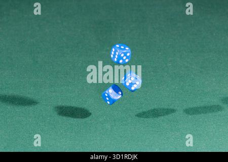 Three blue dices falling on a green table Stock Photo