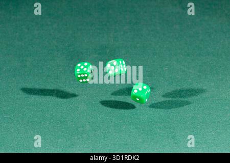 Three green dices falling on a green table Stock Photo