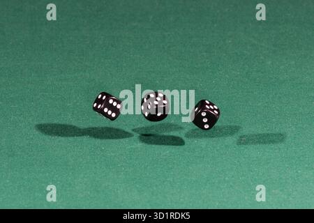 Three black dices falling on a green table Stock Photo