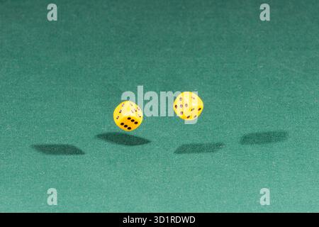 Two yellow dices falling on a green table Stock Photo