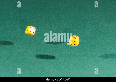 Two yellow dices falling on a green table Stock Photo
