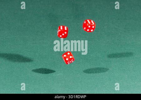 Three red dices falling on a green table Stock Photo