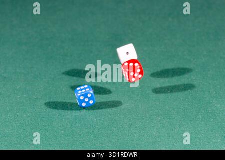 White, red and blue dices falling on a green table Stock Photo