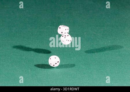 Three white dices falling on a green table Stock Photo
