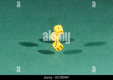 Three yellow dices falling on a green table Stock Photo