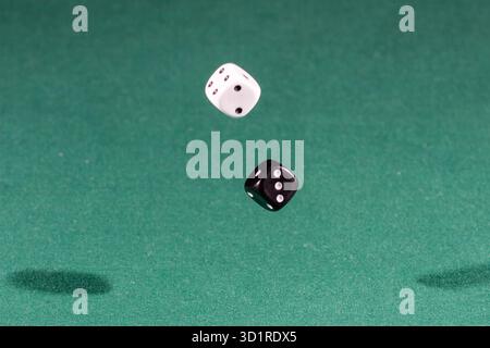 Two white and black dices falling on a green table Stock Photo