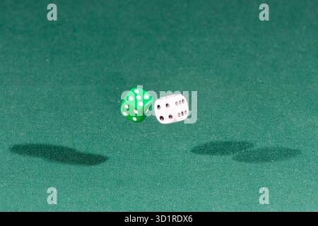 Two white and green dices falling on a green table Stock Photo