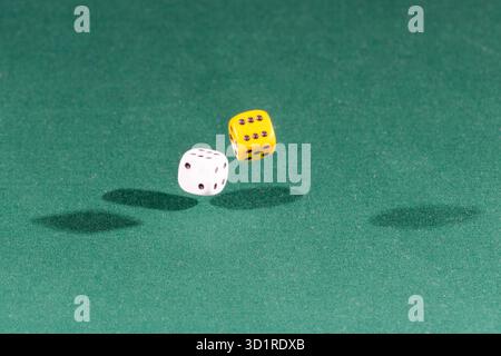 Two white and yellow dices falling on a green table Stock Photo