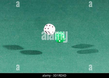 Two white and green dices falling on a green table Stock Photo