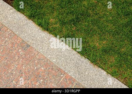 Old red and gray granite pavement and grass in garden decorative texture, line dividing nature and civilization, concept Stock Photo