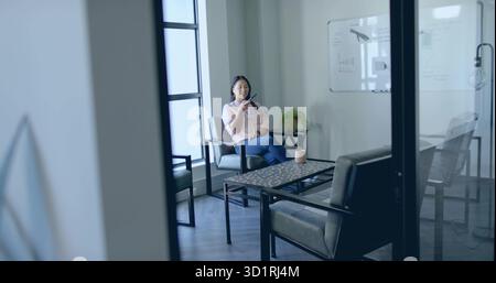 Talking businesswoman speaking into smartphone in meeting lounge, with ceramic mug, copy space Stock Photo