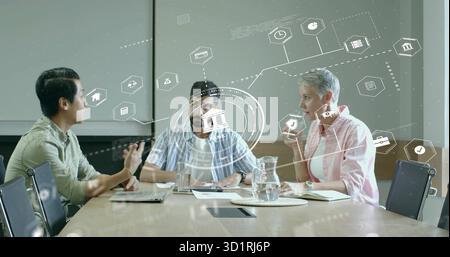 Gesturing Asian man and colleagues collaborating at conference table with laptop finance holograms Stock Photo