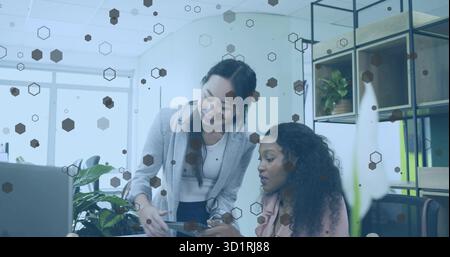 Collaborating office professionals pointing at tablet and reviewing at desk, laptop stylus plant Stock Photo
