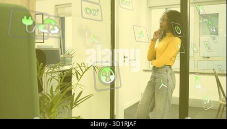 Woman in mustard top analyzing sustainability icons on glass partition in meeting room, copy space Stock Photo