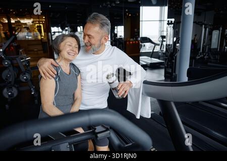 Mature man is hugging his partner while resting in a gym setting Stock Photo