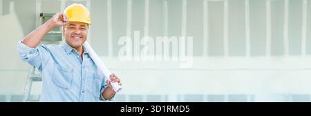 Hispanic Male Contractor Wearing Hard Hat Against Drywall Banner Background with Ladder Stock Photo