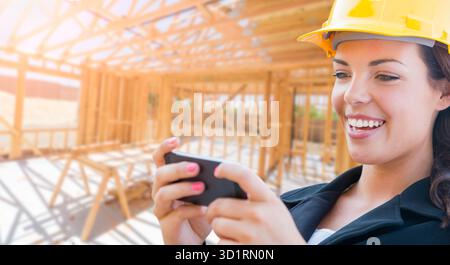Smiling Female Contractor In Hard Hat Using Smart Phone At Construction Site Stock Photo