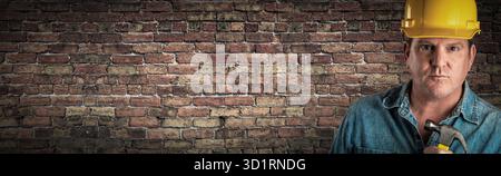 Male Contractor In Hard Hat Holding Hammer In Front Of Old Brick Wall Banner with Copy Space Stock Photo