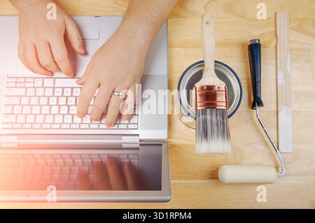Paint Tools Next to Handyman Using Laptop Overhead Stock Photo
