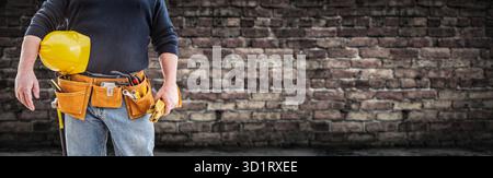 Contractor With Tool Belt and Hard Hat In Front of Aged Brick Wall Banner Stock Photo