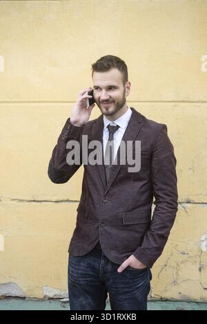 Man in suit talking on mobile phone against the wall Stock Photo