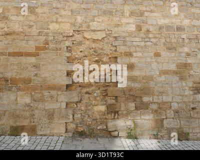 Rough stone wall with light brown blocks, bricked-up opening, and paved walkway. Signs of age and weathering visible. Copyspace. Stock Photo