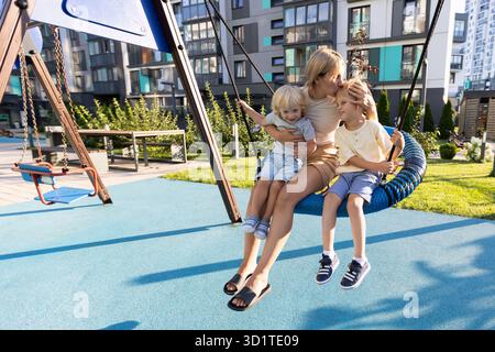 Mother Enjoys Quality Time With Her Two Sons On Playground Swings Stock Photo