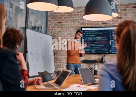 In a corporate setting businessman leads a meeting, passionately presenting a business plan to his attentive team, fostering col Stock Photo