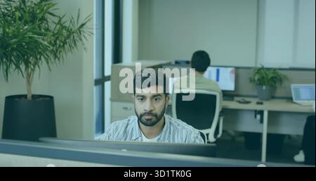 Working man wearing striped shirt sitting at desk in open-plan office, with desktop monitor Stock Photo