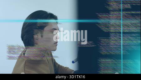 Programmer in brown jacket examining glitchy code on monitor in workspace, with blue-capped stylus Stock Photo