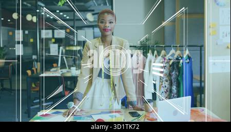 Female fashion designer arranging pattern sheets in studio, with measuring tape and fabric swatches Stock Photo