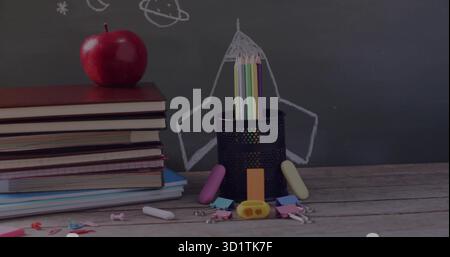 Holding colored pencils, pencil holder sitting in class with apple-topped textbooks and chalkboard Stock Photo