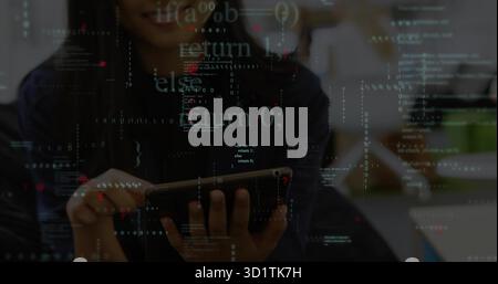 Analyzing code, developer wearing dark top using tablet at office desk, monitors and code overlay Stock Photo