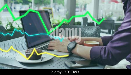 Typing mature Asian man focusing on laptop in coffee shop, with coffee cup, muffin, smartphone Stock Photo