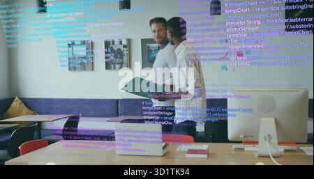Discussing software tasks coworkers standing at table in office, with laptop and code overlay Stock Photo