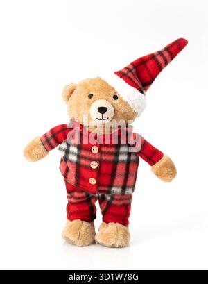 A cute plush teddy bear in red plaid Christmas pajamas and a tall Santa hat, standing isolated on a white background Stock Photo