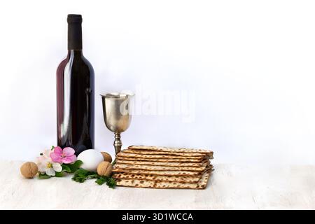 Matzo, wine, silver bowl, pink flowers apple tree, white egg and walnuts for passover celebration on white wooden table on light background with space Stock Photo