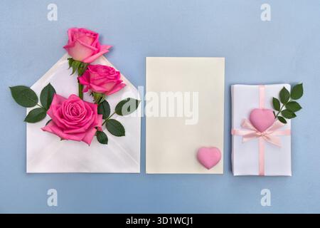 Pink flowers roses postal envelope with paper card note with space for text, pink hearts on a blue background. Top view, flat lay Stock Photo