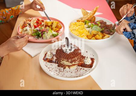 Females having brunch steak and egg, tacos with desserts. Stock Photo