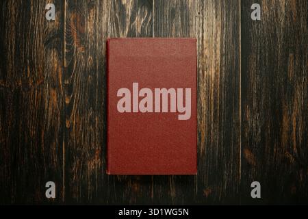 Blank burgundy book cover centered on a rich, dark, rustic wooden background. Stock Photo
