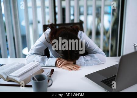 Alone Working Late. Asian business woman at workplace in office  laid her head down on the table fell asleep in front of lapto Stock Photo