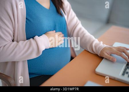 Pregnant asian woman using laptop at home pregnant businesswoman typing on laptop working on remote project in home office pre Stock Photo