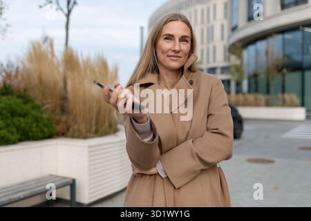 A business woman stands in front of a business center while looking at her phone Stock Photo