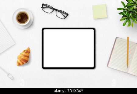 Tablet with blank screen on a white desk, coffee, croissant, notebook, and glasses, perfect for branding and creative design Stock Photo