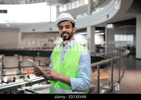 Construction Worker in Safety Gear Using Tablet to Manage Project Details in Modern Building Stock Photo